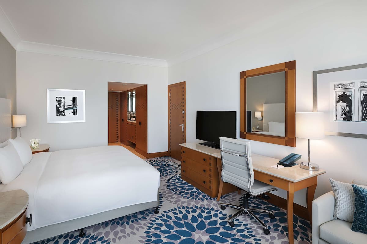 A hotel room with a large bed, a desk with a computer, a TV, and a mirror.