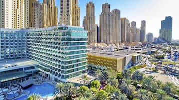 A modern hotel with multiple floors, a rooftop pool, and a landscaped area with palm trees.