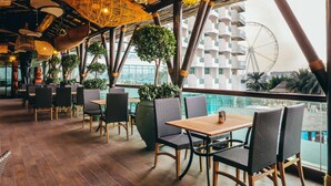 An indoor dining area with wooden tables and chairs, hanging wicker lamps, and a view of a Ferris wheel. - Hilton Dubai Jumeirah (Dubai)
