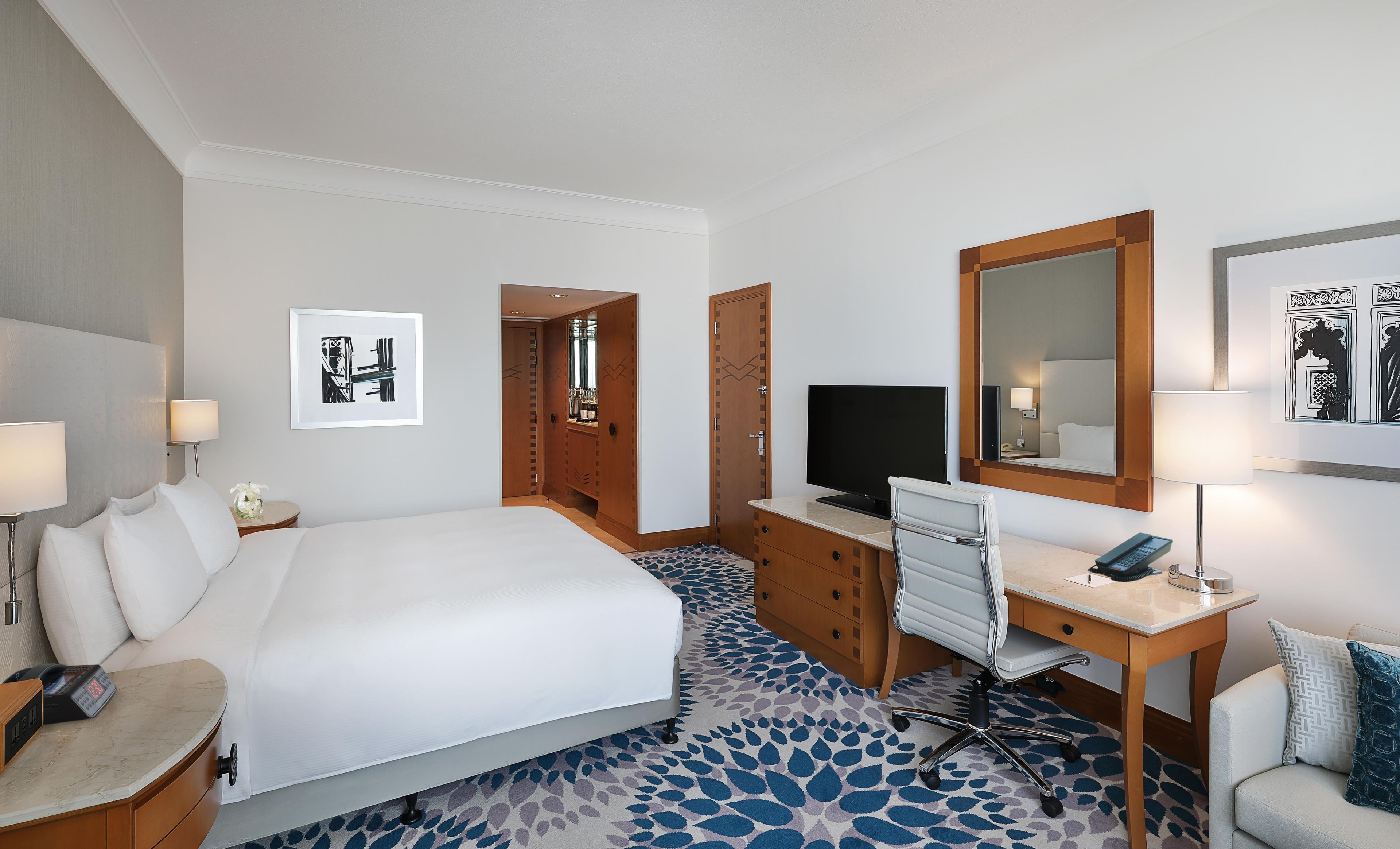 A hotel room with a bed, desk, TV, and a mirror.