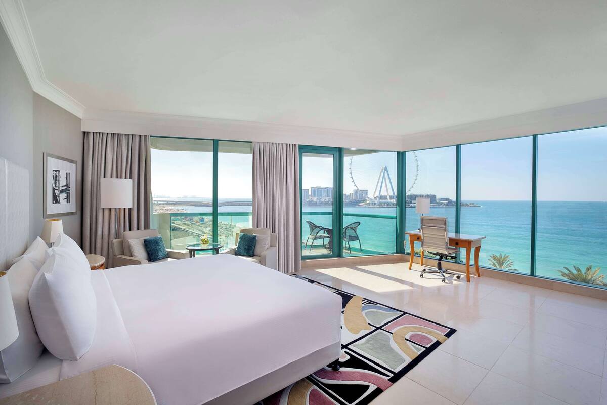 A hotel room with a large bed, a desk, and a view of the ocean and a bridge.