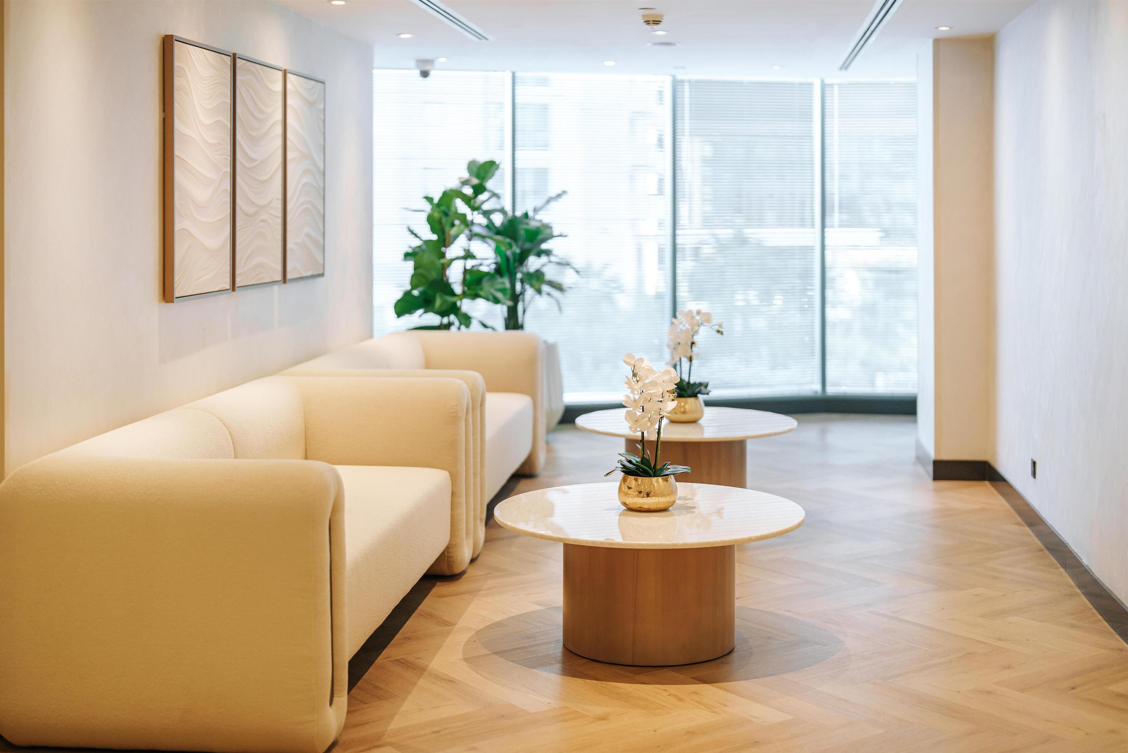 Un hall d’hôtel moderne, doté d’un ensemble de canapés, de deux tables rondes et de grandes fenêtres donnant sur la ville.