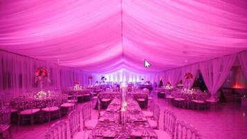 A banquet hall with tables set for a formal event, draped with pink fabric, and a central aisle leading to a stage.