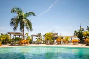A pool area with lounge chairs, palm trees, and covered seating areas.