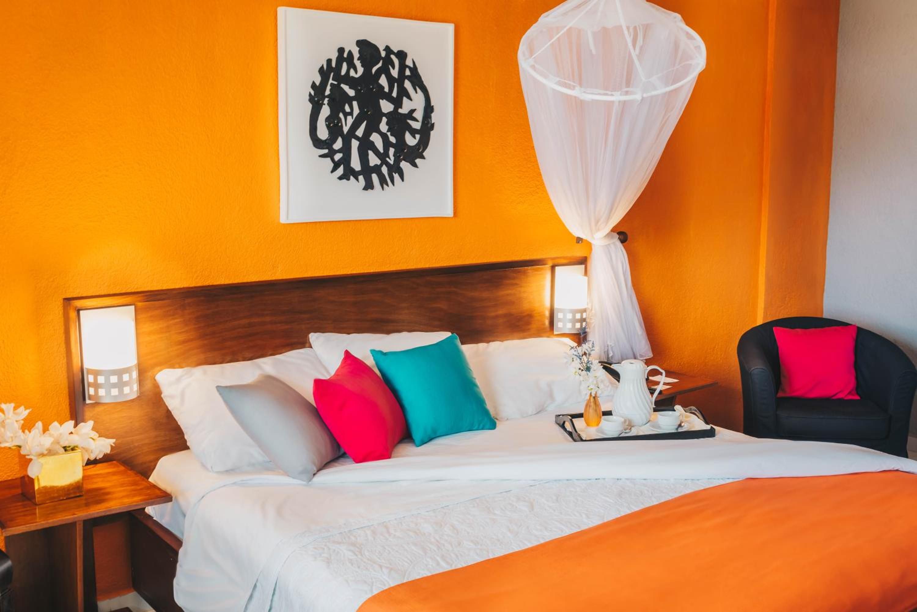 A hotel room with a bed, a bedside table, a chair, a nightstand, a wall-mounted artwork, and a canopy bed.