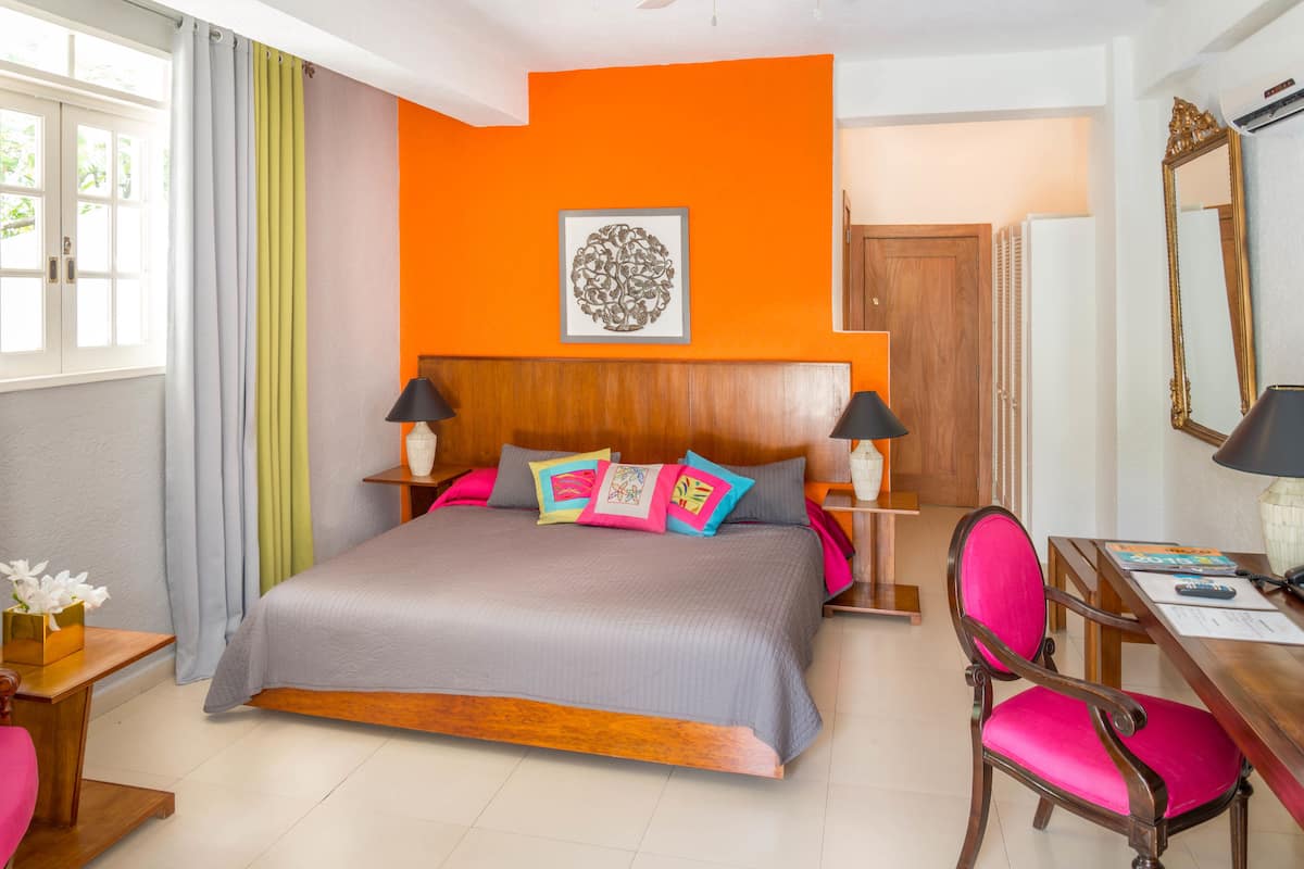 Una habitación de hotel con una cama grande, dos mesitas de noche con lámparas, un escritorio con una silla y un espejo grande.