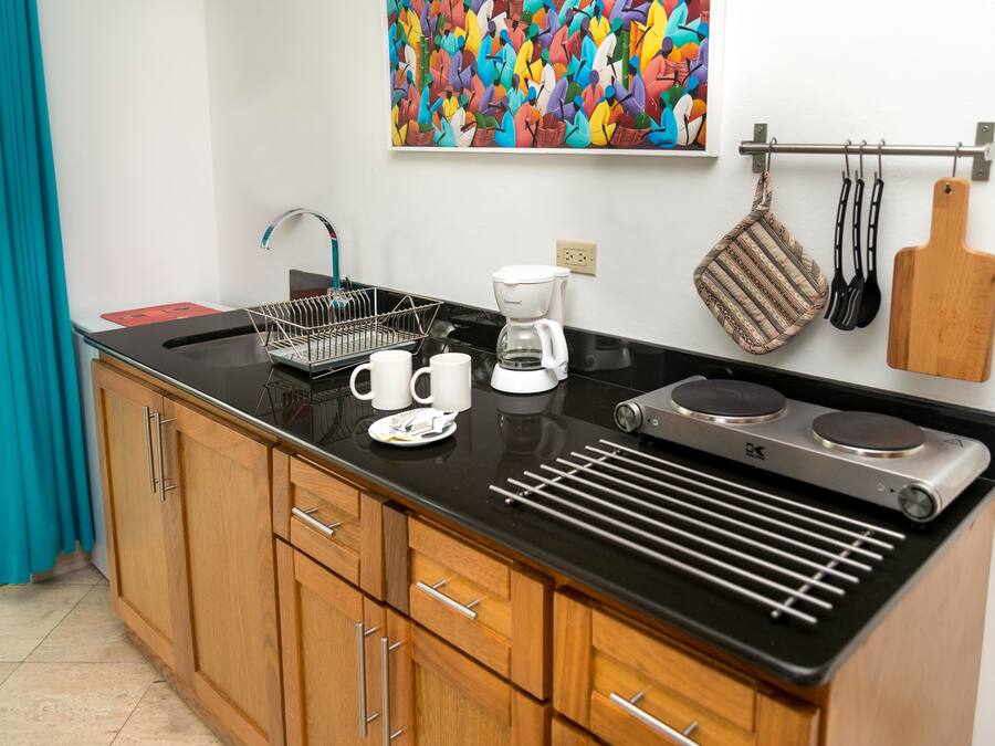 Una cocina moderna con armarios de madera, encimera negra, cafetera y un colorido cuadro abstracto en la pared.