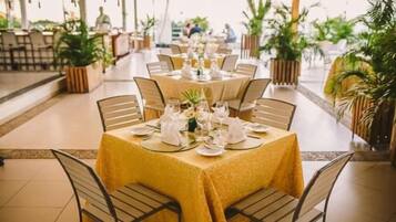 A dining area with round tables set for multiple guests, each table with a yellow tablecloth and white tableware.