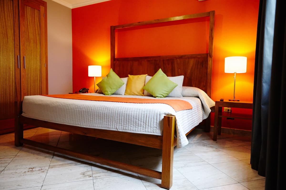 Una cama grande con estructura de madera y ropa de cama blanca, dos lámparas de noche y una mesita de noche con un teléfono.