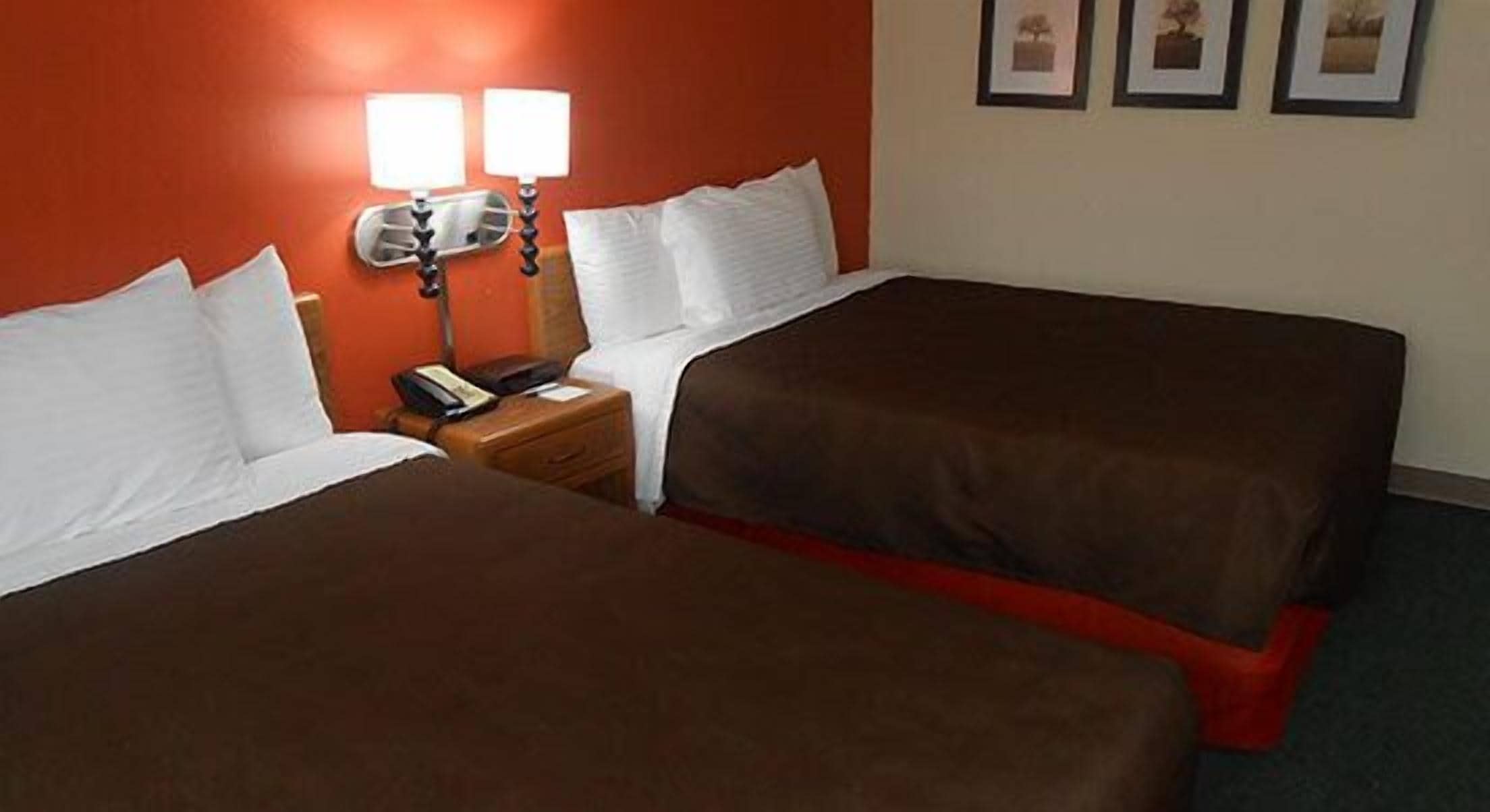 A hotel room with two beds, a nightstand with a phone, and a wall-mounted lamp.