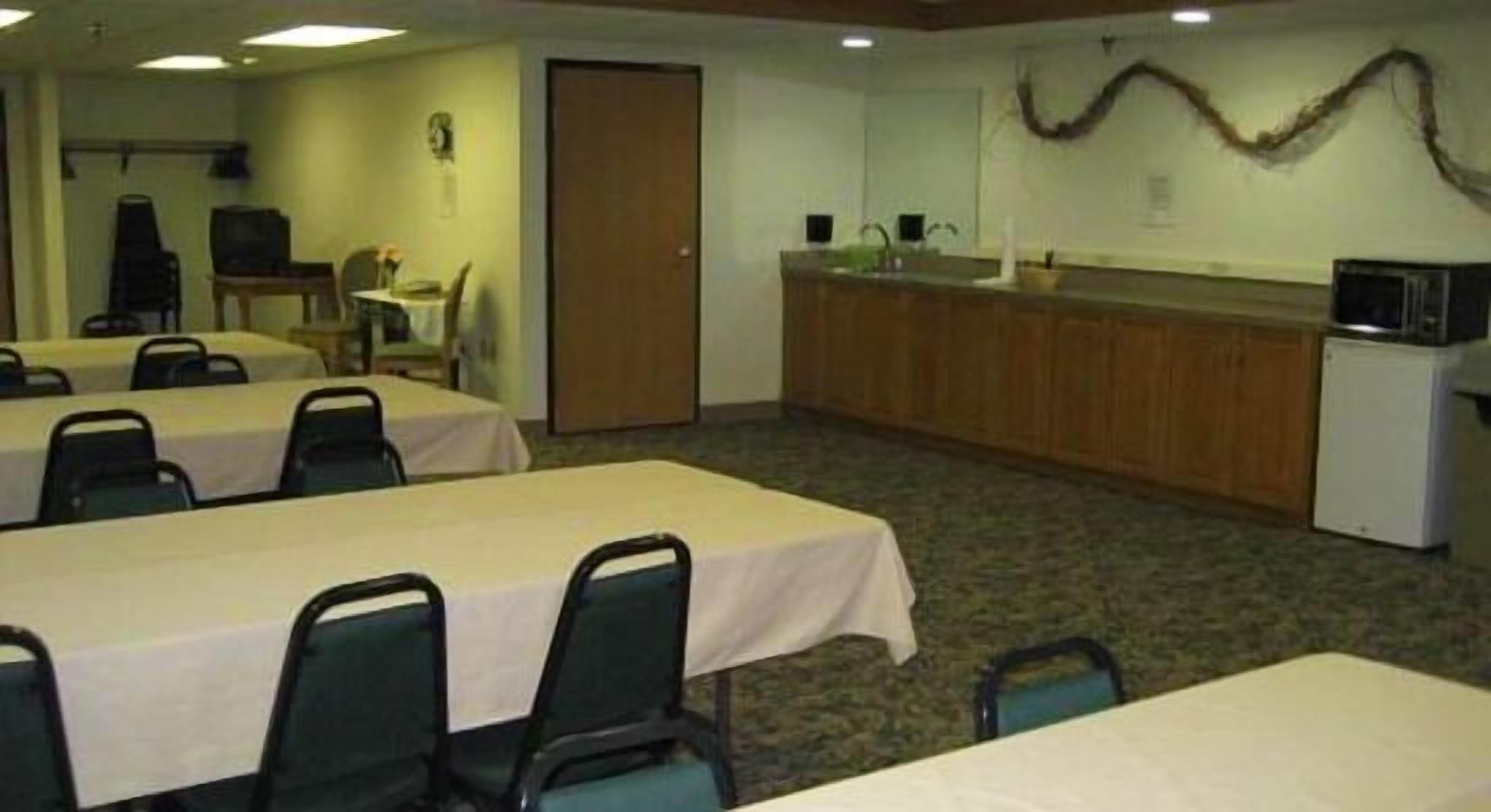 A conference room with tables and chairs, a kitchenette, and a door.