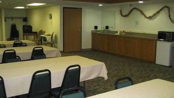 Un salón de conferencias con mesas, sillas, una kitchenette y una puerta.