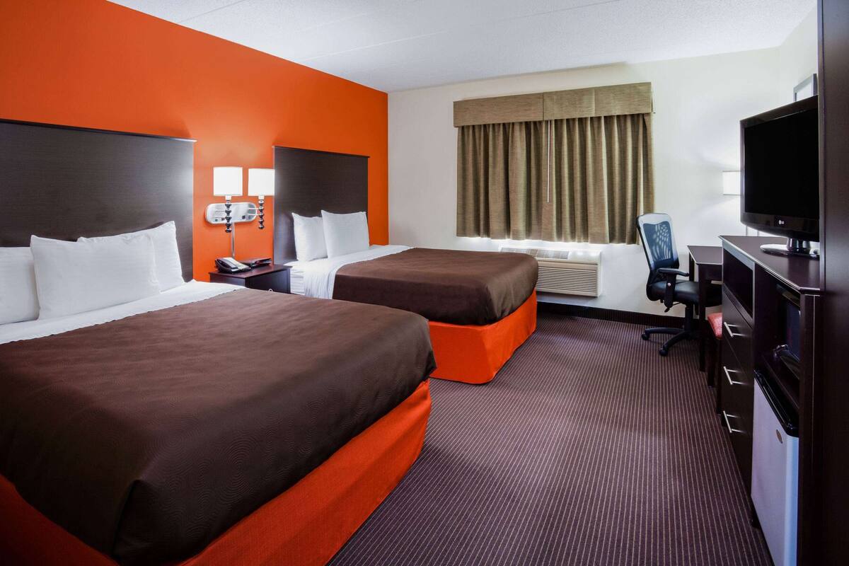 A hotel room with two beds, a TV, a desk, and a chair.