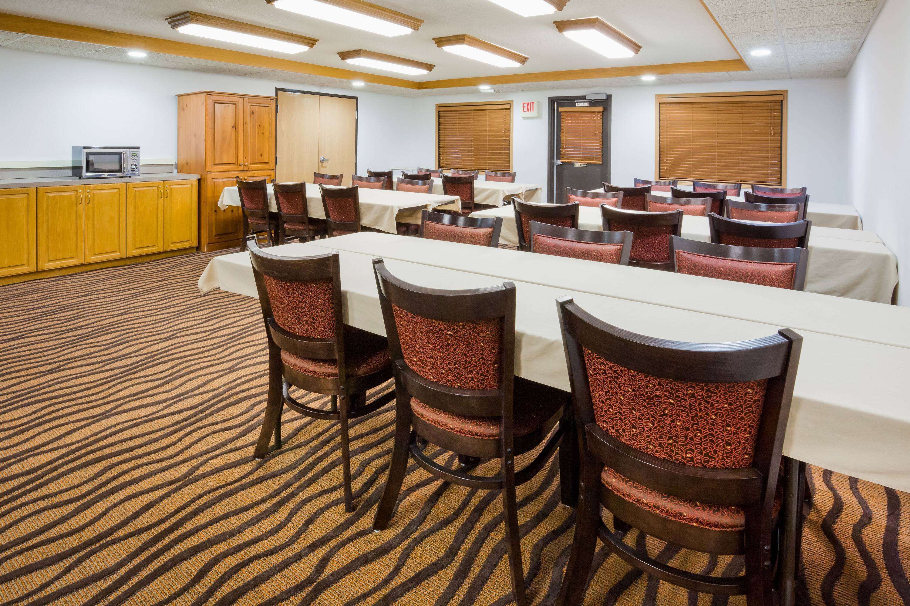 A conference room with a long table, multiple chairs, wooden cabinets, and a carpeted floor.