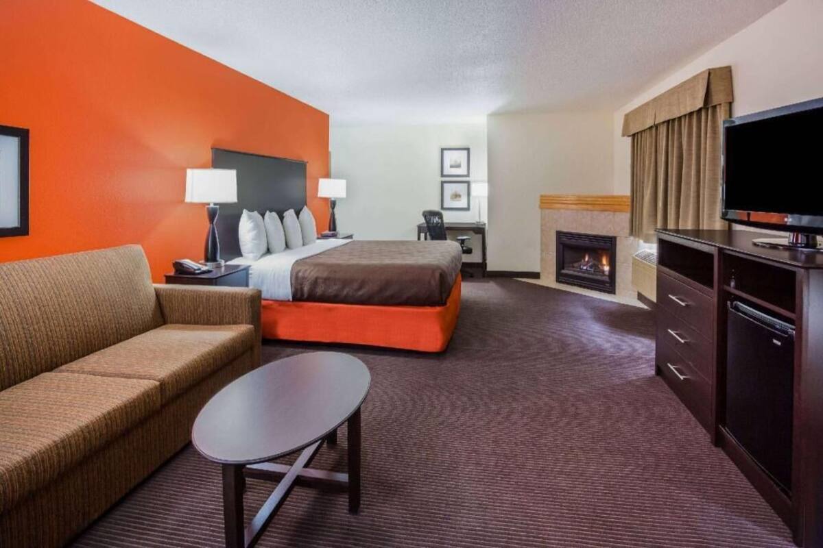 A hotel room with a bed, a sofa, a small table, a TV, a fireplace, and a desk with a chair.