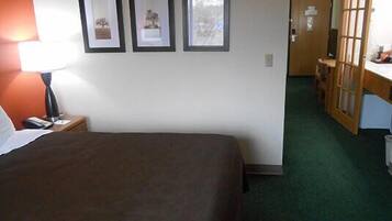 A hotel room with a bed, a desk, a chair, a lamp, and framed pictures on the wall.