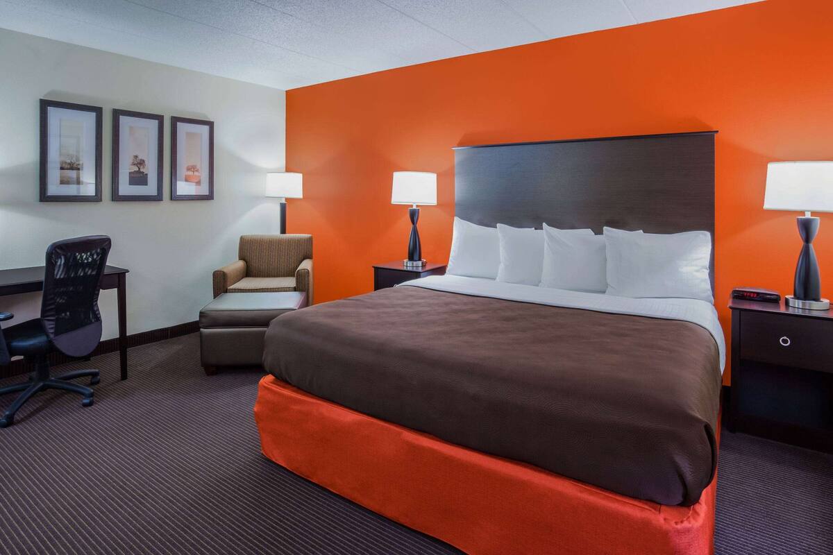 A hotel room with a large bed, two bedside tables with lamps, a desk, a chair, and framed pictures on the wall.