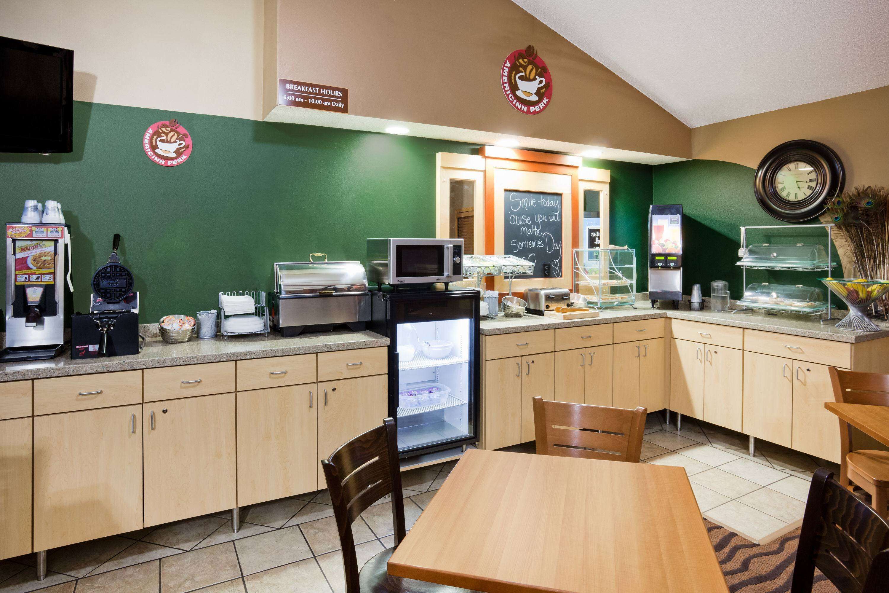 Una cafetería con armarios de madera, un microondas, un refrigerador, una cafetera y una pizarra con un mensaje.