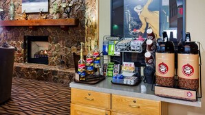 A bar area with a stone wall, a fireplace, and a coffee station with Torani syrup bottles and coffee machines. - AmericInn by Wyndham Mora (Mora)