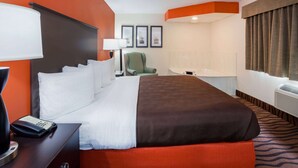 A hotel room with a large bed, a desk with a telephone, a chair, and a window with curtains. - AmericInn by Wyndham Mora (Mora)