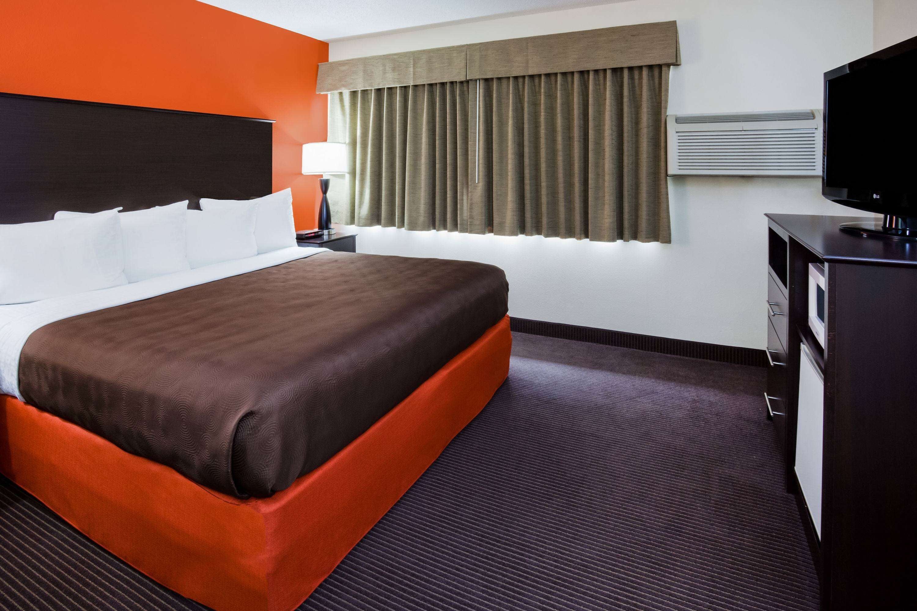 A hotel room with a large bed, a desk with a television, and a window with curtains.