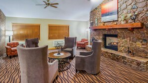 A cozy lounge area with a stone fireplace, comfortable seating, and a patterned carpet. - AmericInn by Wyndham Mora (Mora)