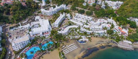 An aerial view of a resort with multiple buildings, a central swimming pool, and a beach area.