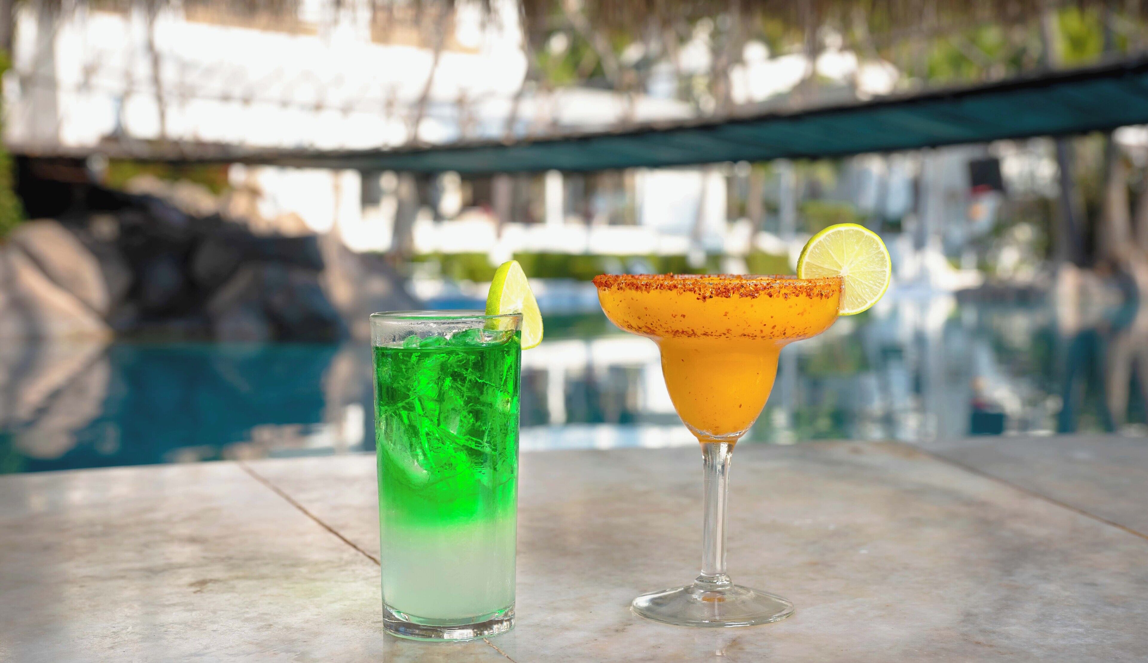 Two drinks on a table by a poolside.