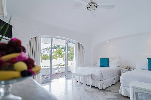 A hotel room with two beds, a ceiling fan, and a balcony with a view of palm trees and buildings. - Las Hadas By Brisas (Manzanillo)