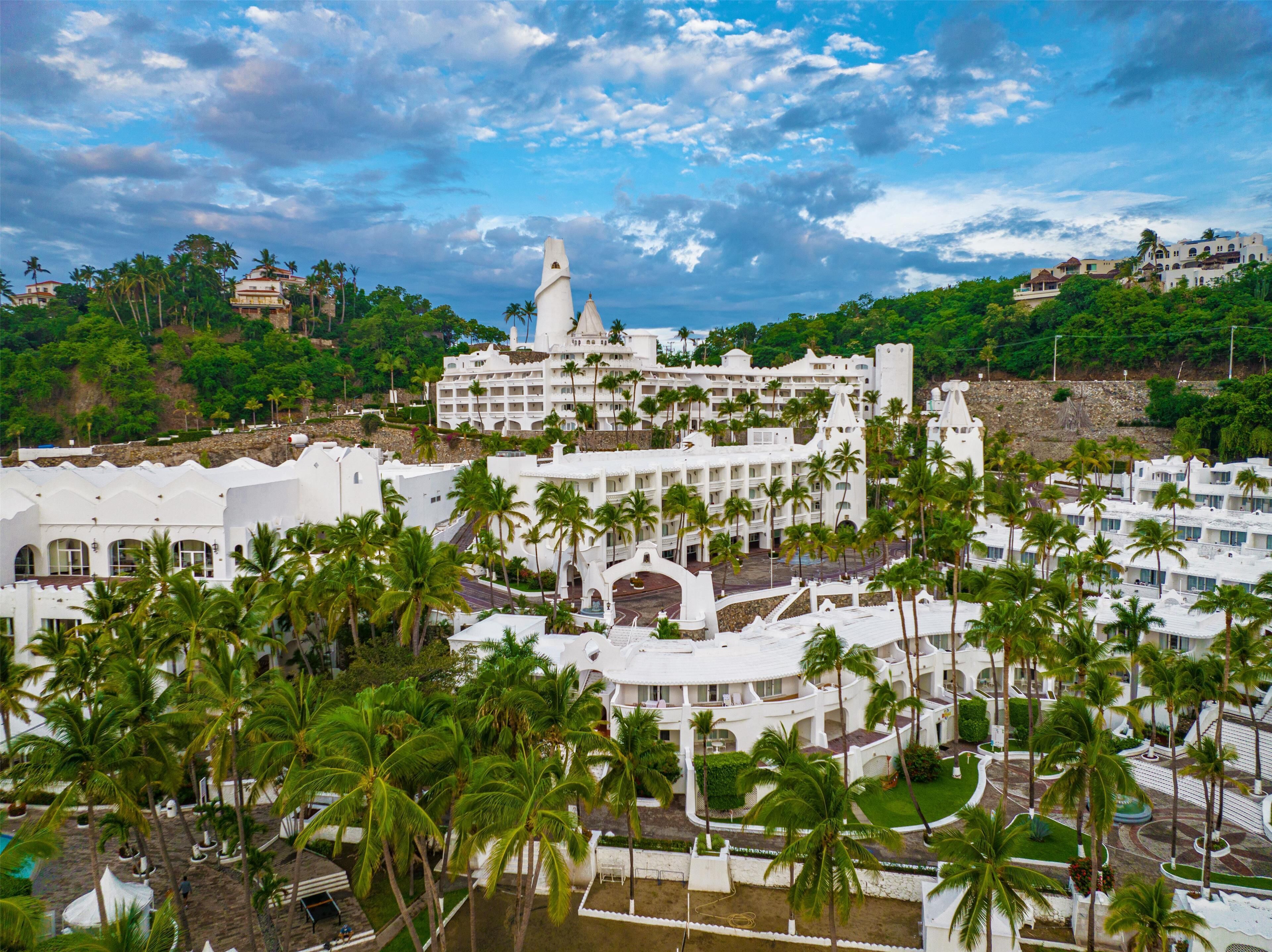 Un resort con varias edificaciones blancas, palmeras y una estructura central grande con techo puntiagudo.
