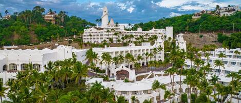 Un resort con varias edificaciones blancas, palmeras y una estructura central grande con techo puntiagudo.