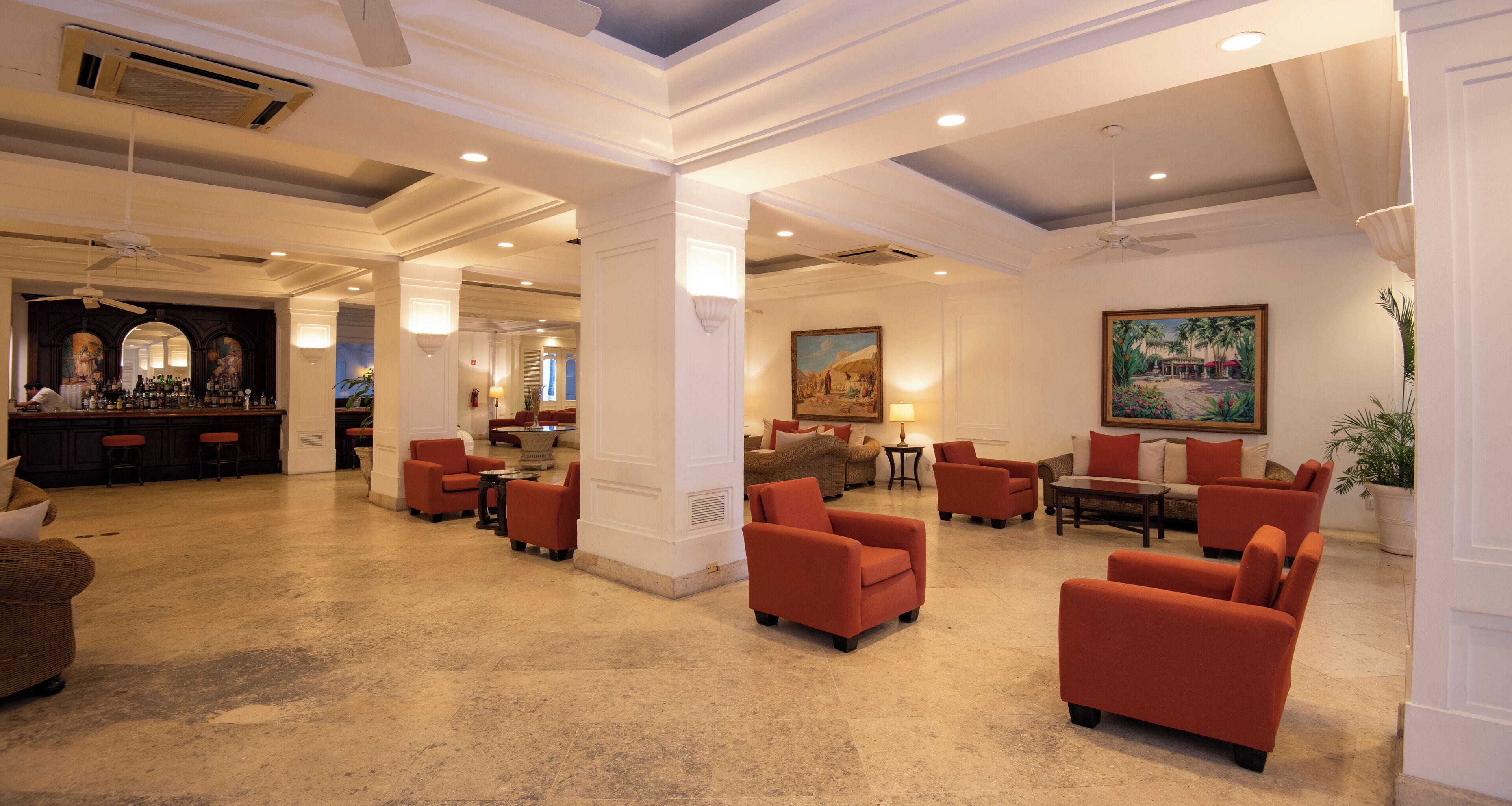 Un hall d’entrée spacieux avec des fauteuils rouges, un coin bar et un tableau accroché au mur.