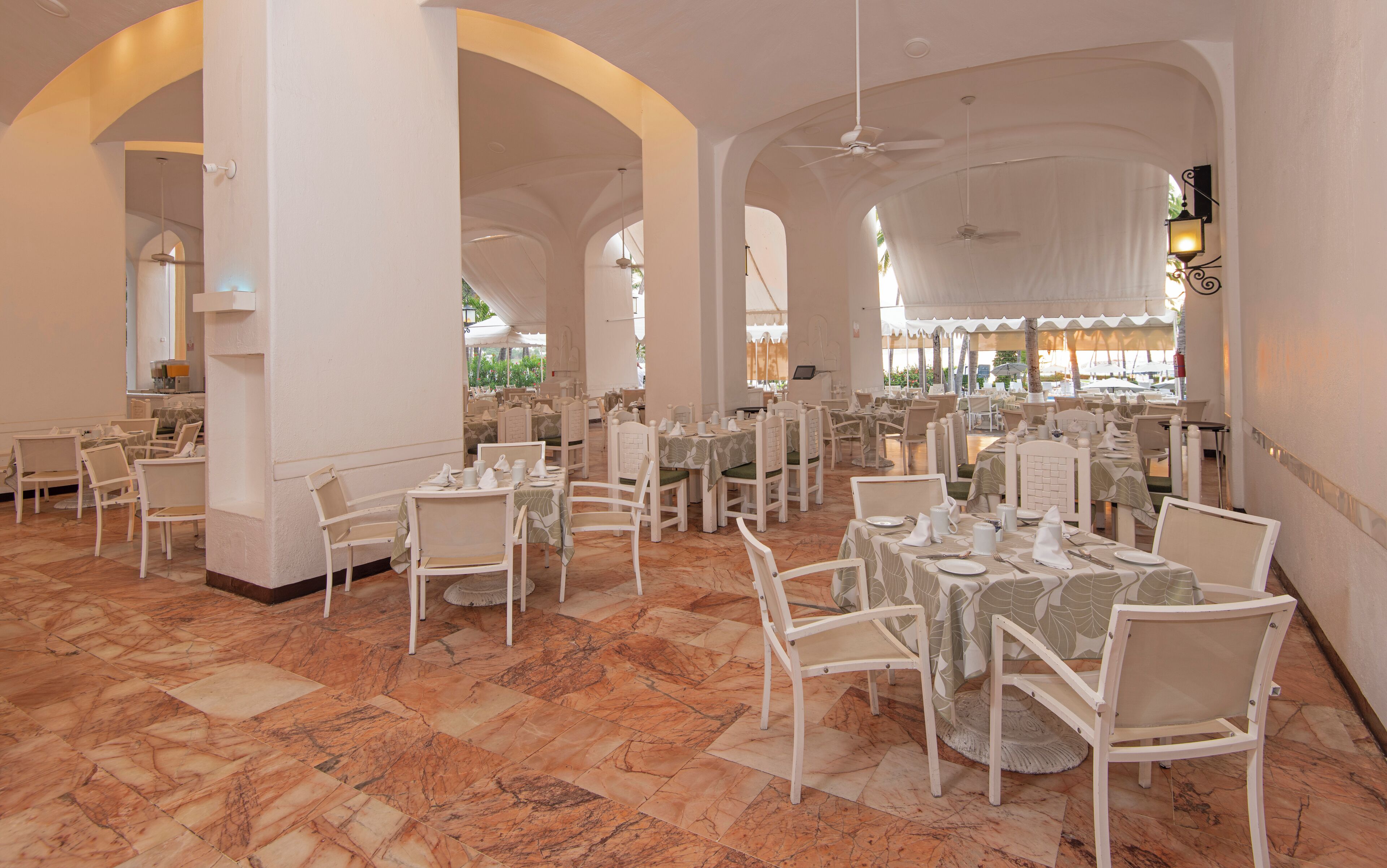 A spacious dining area with white tables and chairs, marble flooring, and large columns.