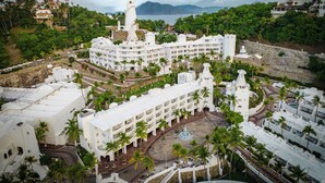 A resort with multiple white buildings, palm trees, and a large body of water in the background. - Las Hadas By Brisas (Manzanillo)