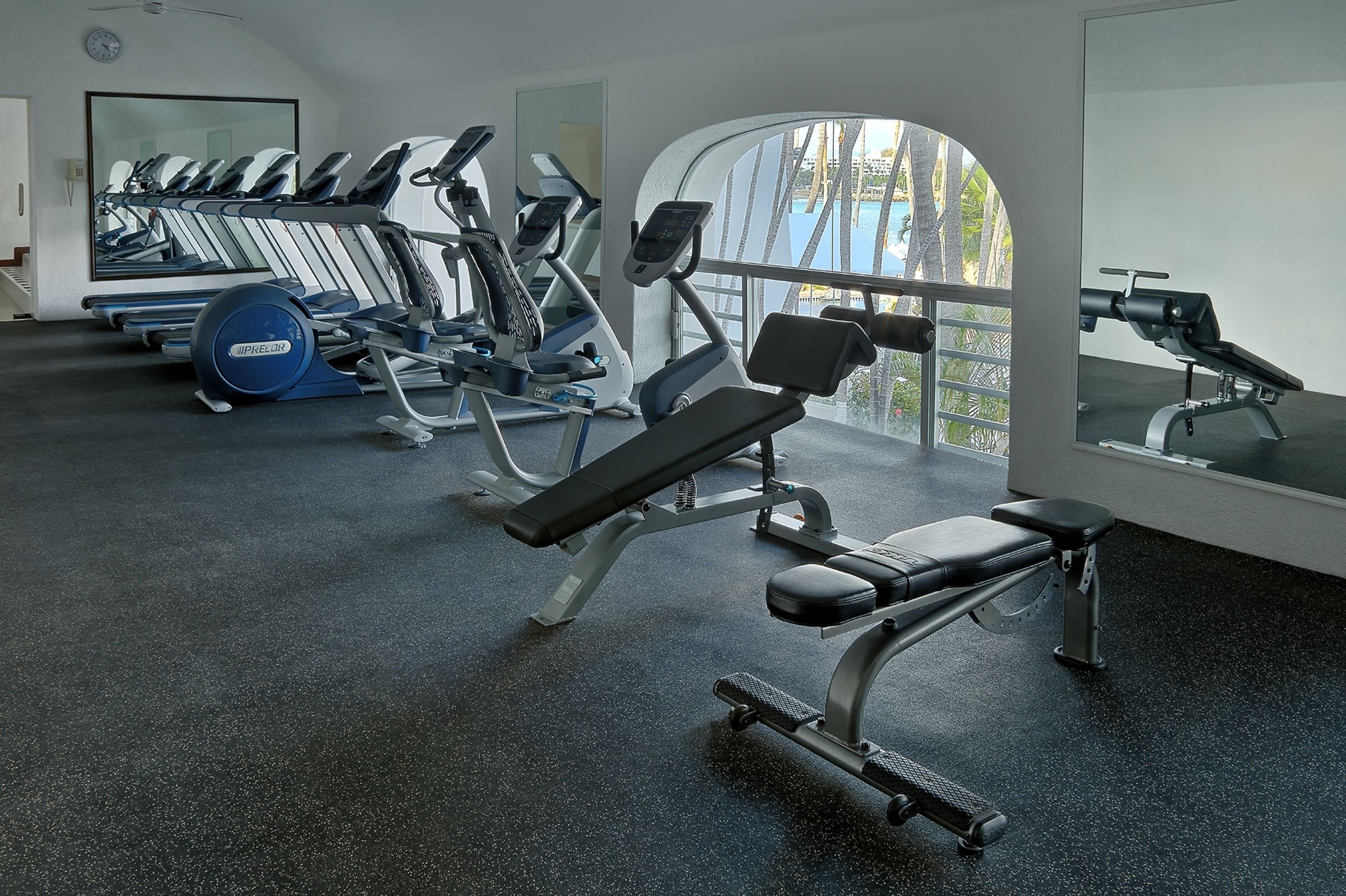 A gym with various exercise equipment, a bench press, and a large mirror.