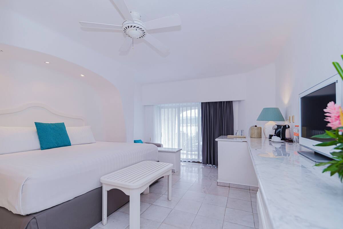 Habitación de hotel moderna con cama, escritorio, televisor y ventilador de techo.
