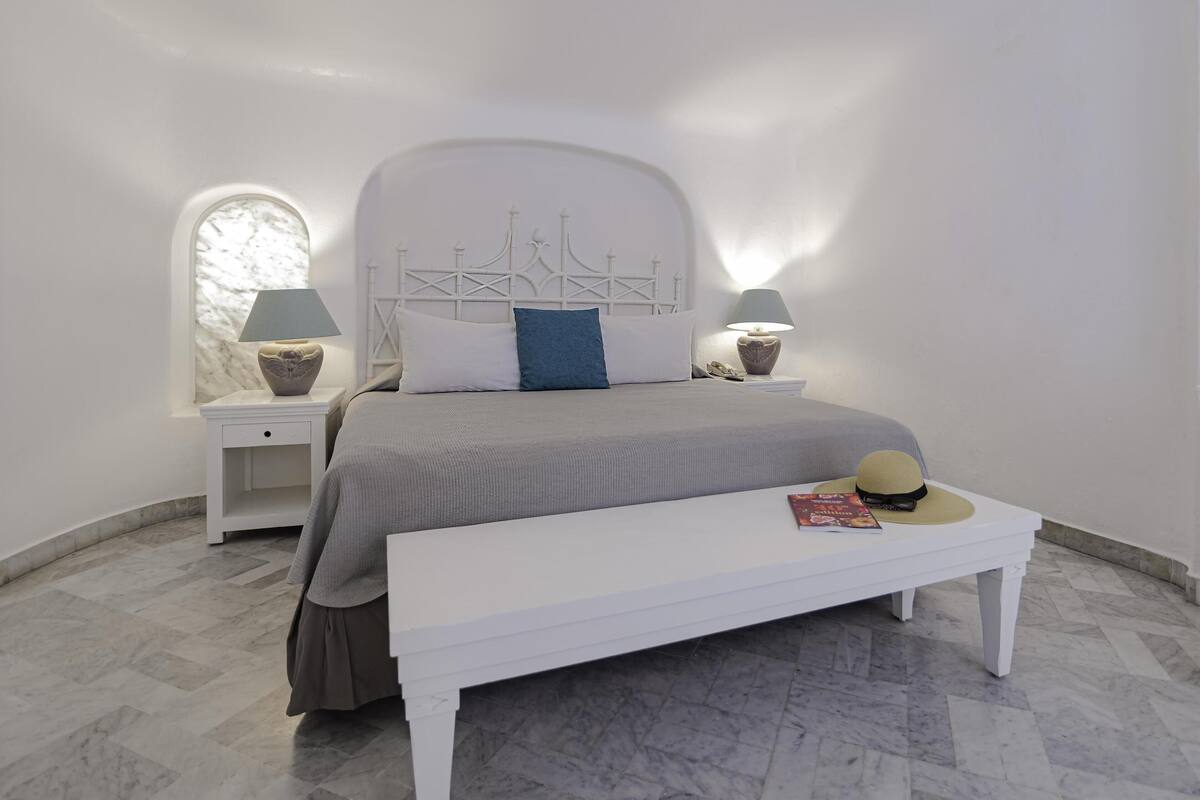 Un dormitorio con cama, dos mesitas de noche con lámparas, un banco y una ventana con vistas.