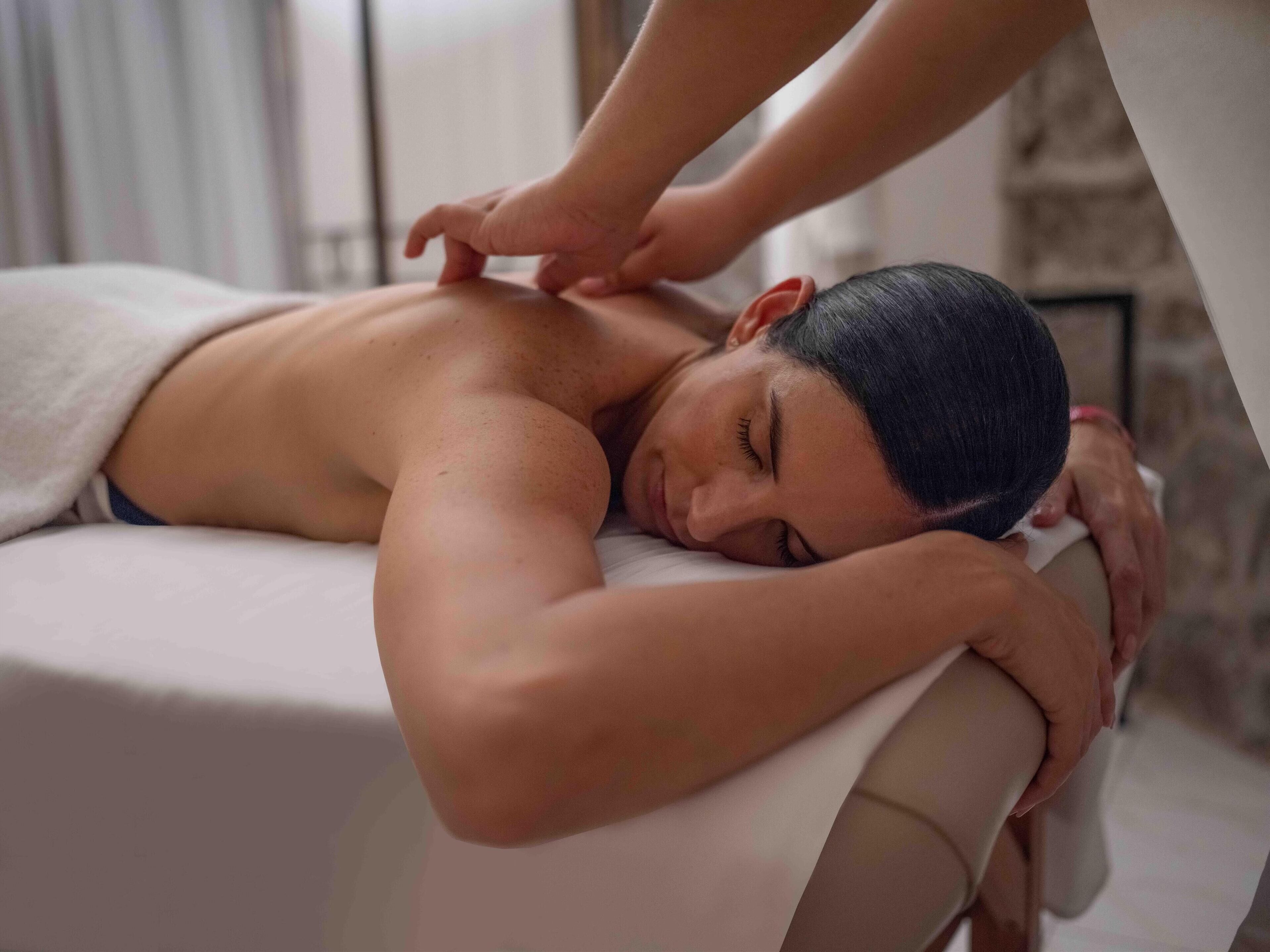 A person receiving a massage in a room with a stone wall and a window.