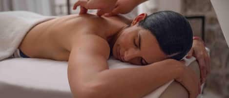 A person receiving a massage in a room with a stone wall and a window.