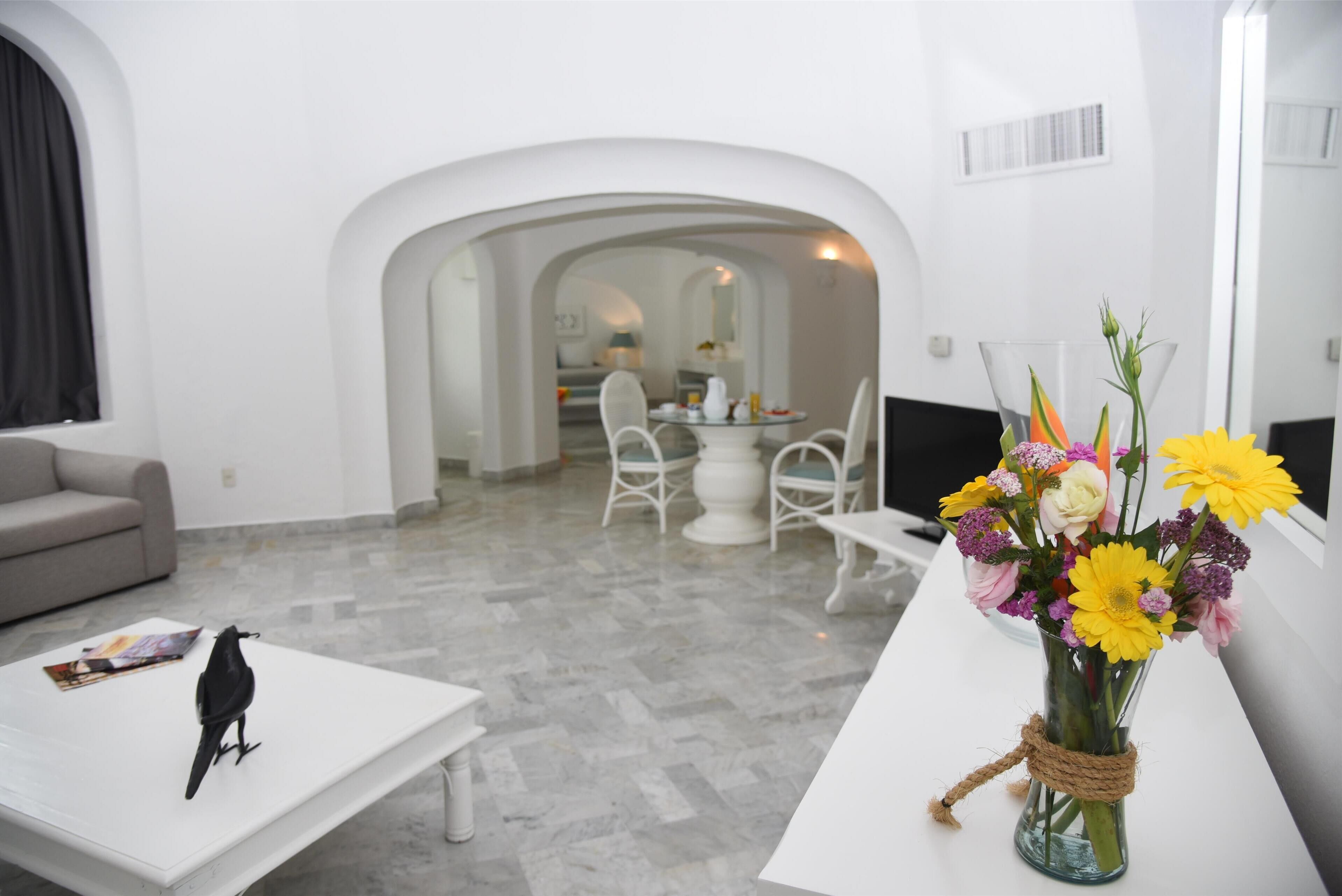 A modern living room with a white sofa, a coffee table with a magazine, a black bird figurine, and a vase of flowers.