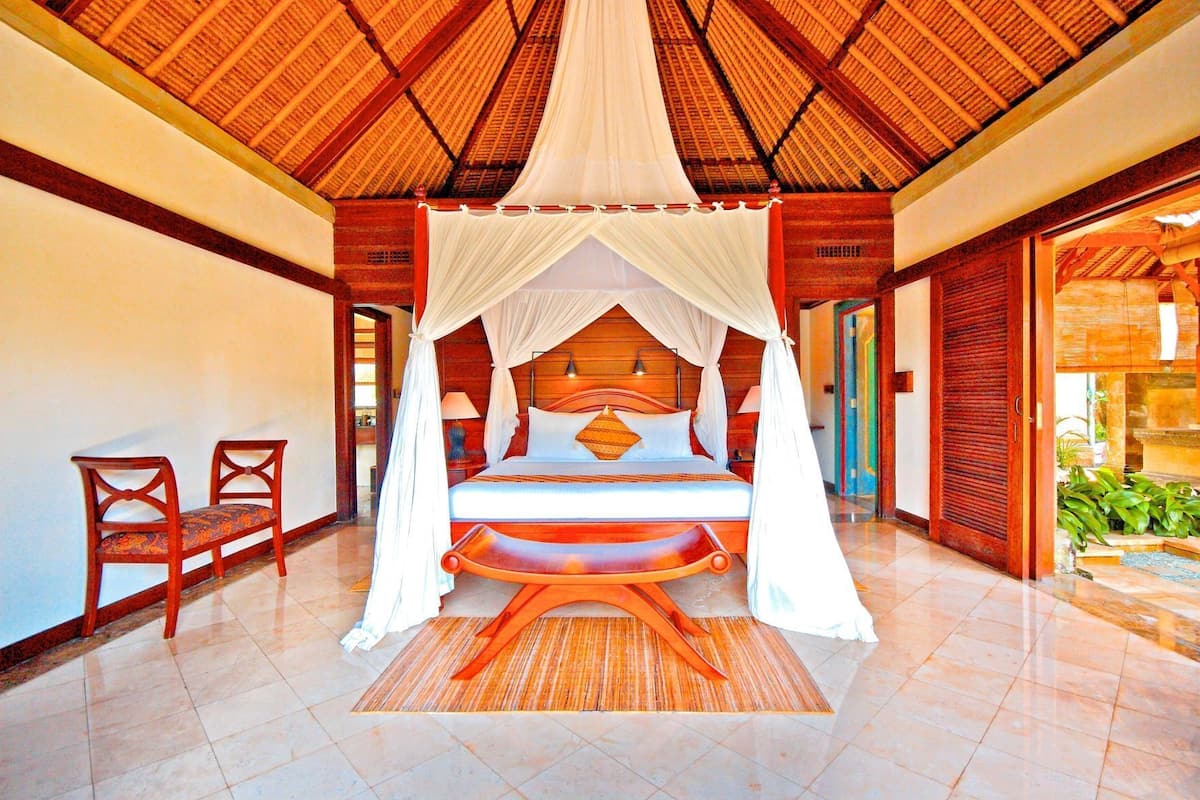 A four-poster bed with a canopy, wooden furniture, and a tiled floor.