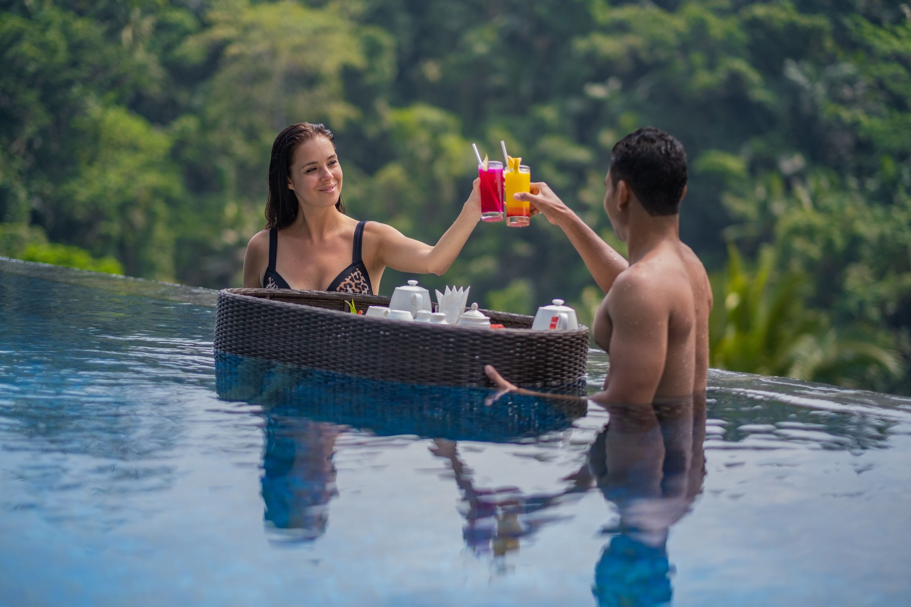 Dos personas en una piscina con un bote de mimbre que contiene un juego de té y vasos.