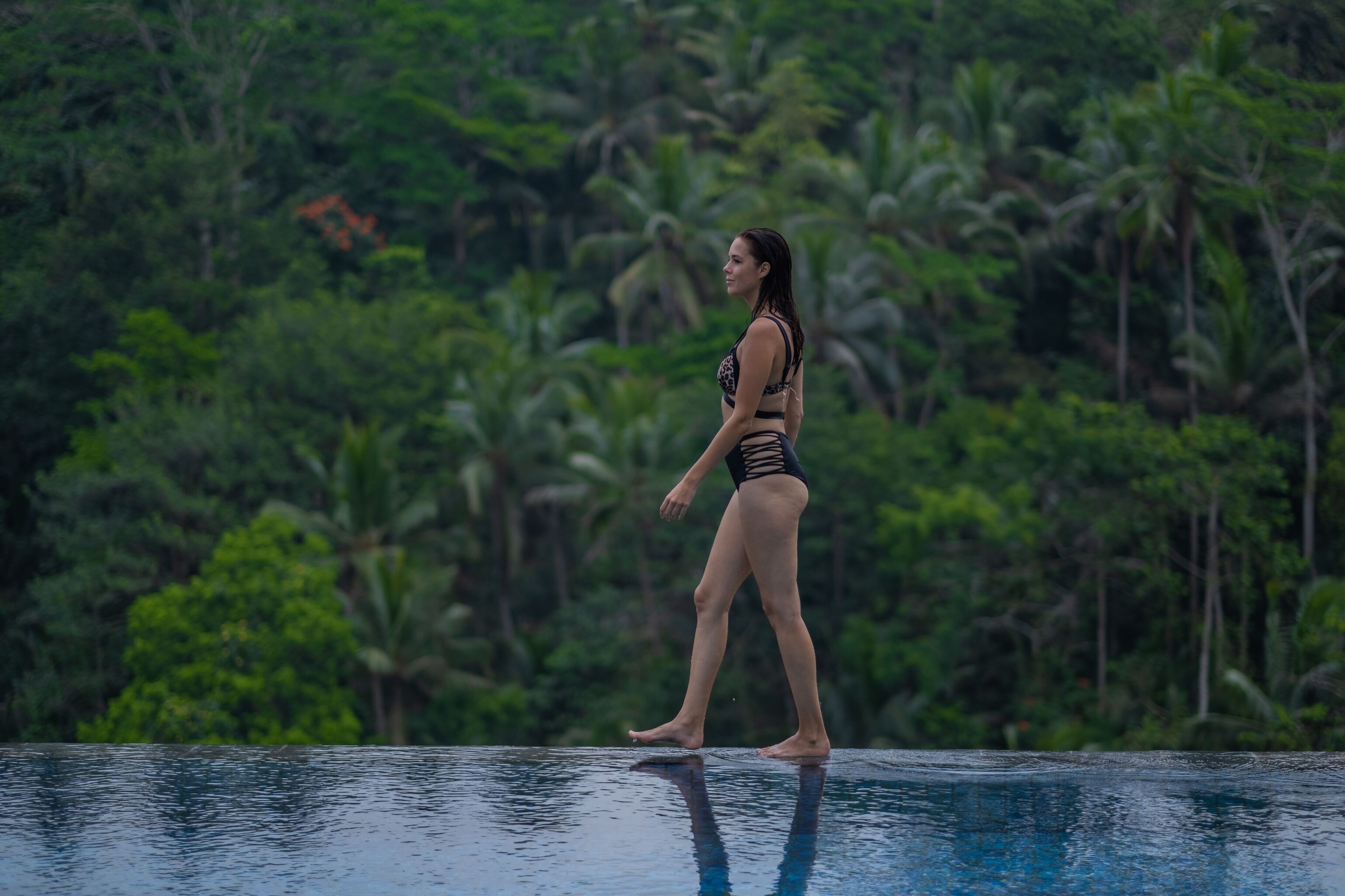 A person standing on a pool edge with a lush green background.