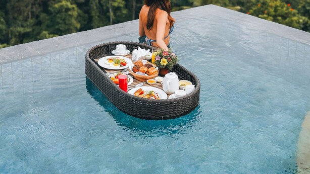 A person sitting on a floating platform in a pool with a basket of food and drinks, surrounded by lush greenery. - Puri Wulandari a Boutique Resort and Spa (Ubud)
