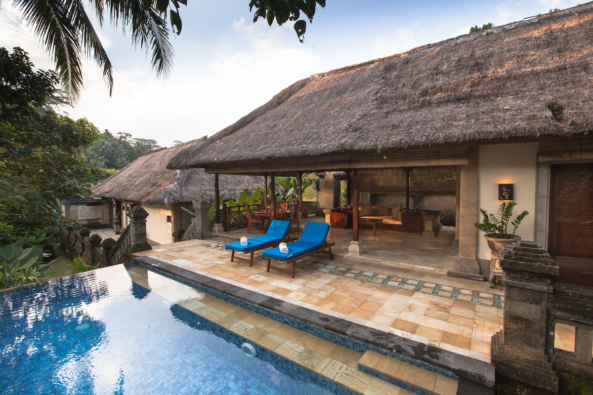 A poolside area with two lounge chairs, a thatched-roof structure, and a tiled pool.