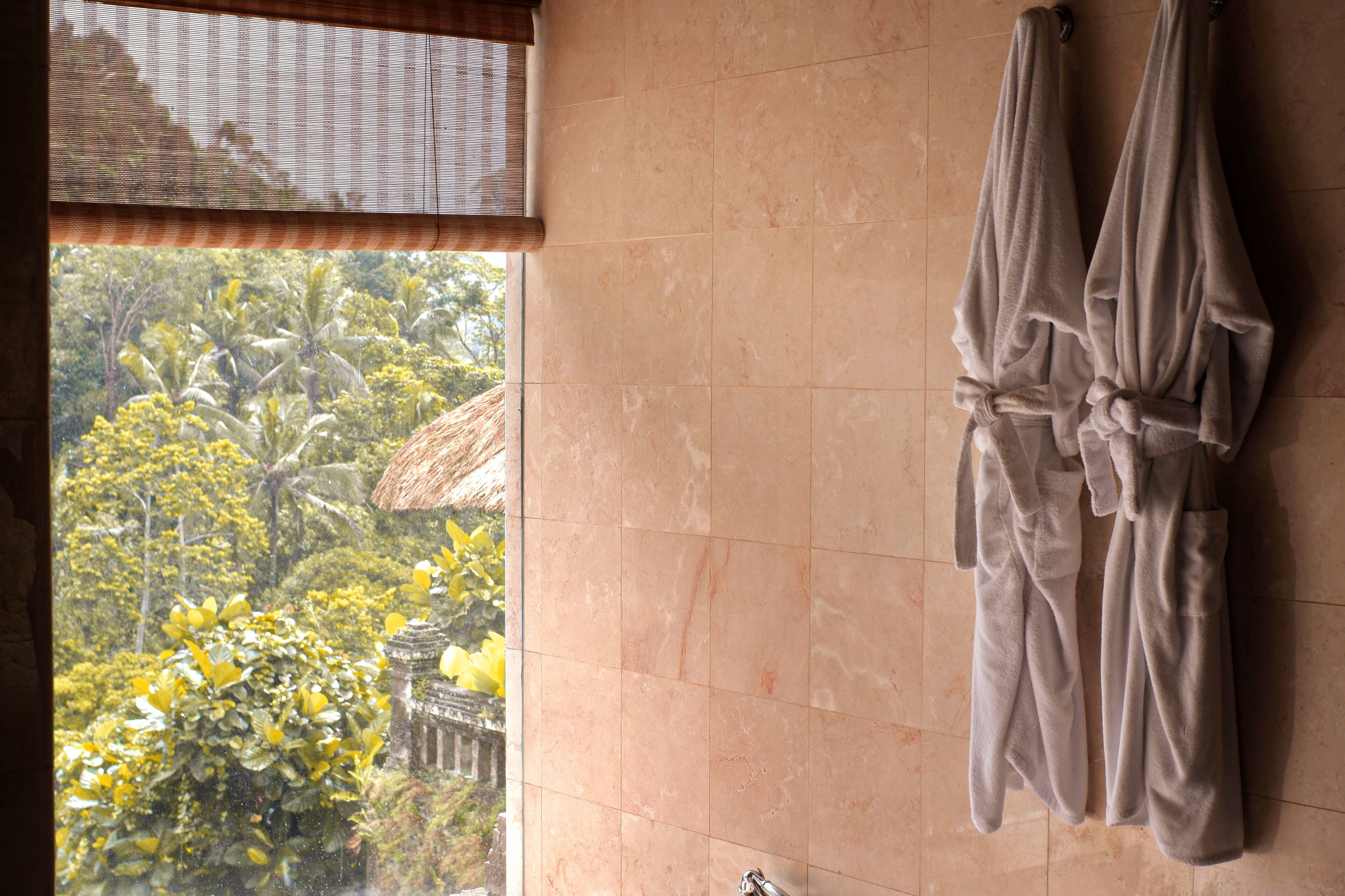 A bathroom with a large window, a tiled wall, and two towels hanging on hooks.