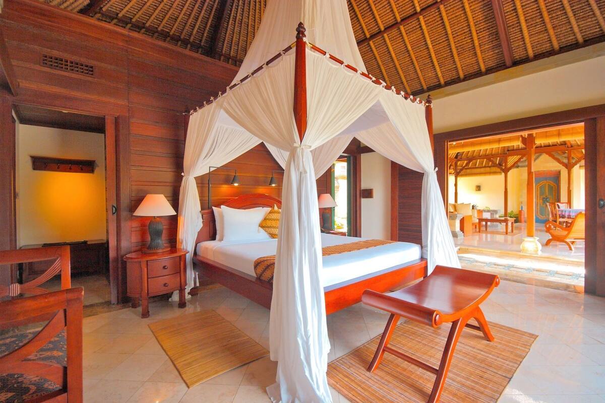 A four-poster canopy bed with a wooden headboard, bedside tables, and a bench.
