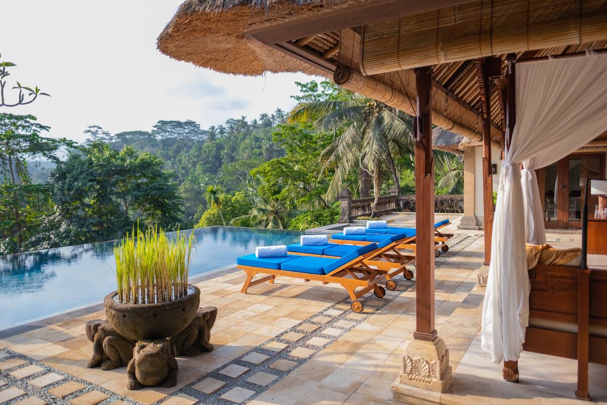 A poolside area with lounge chairs, a thatched roof, and a view of a lush landscape.