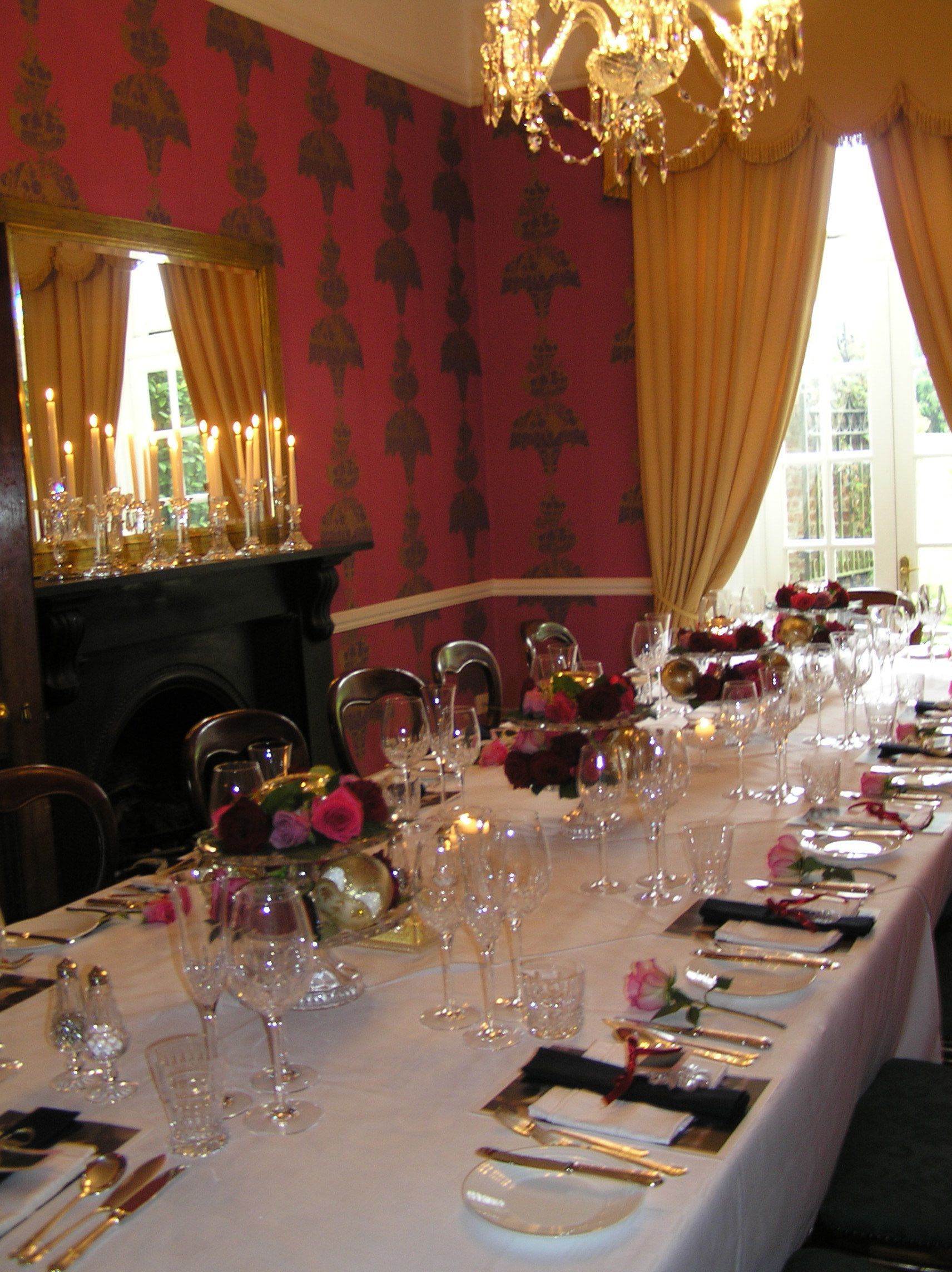 A formal dining room with a long table set for a meal, candles, and a chandelier.