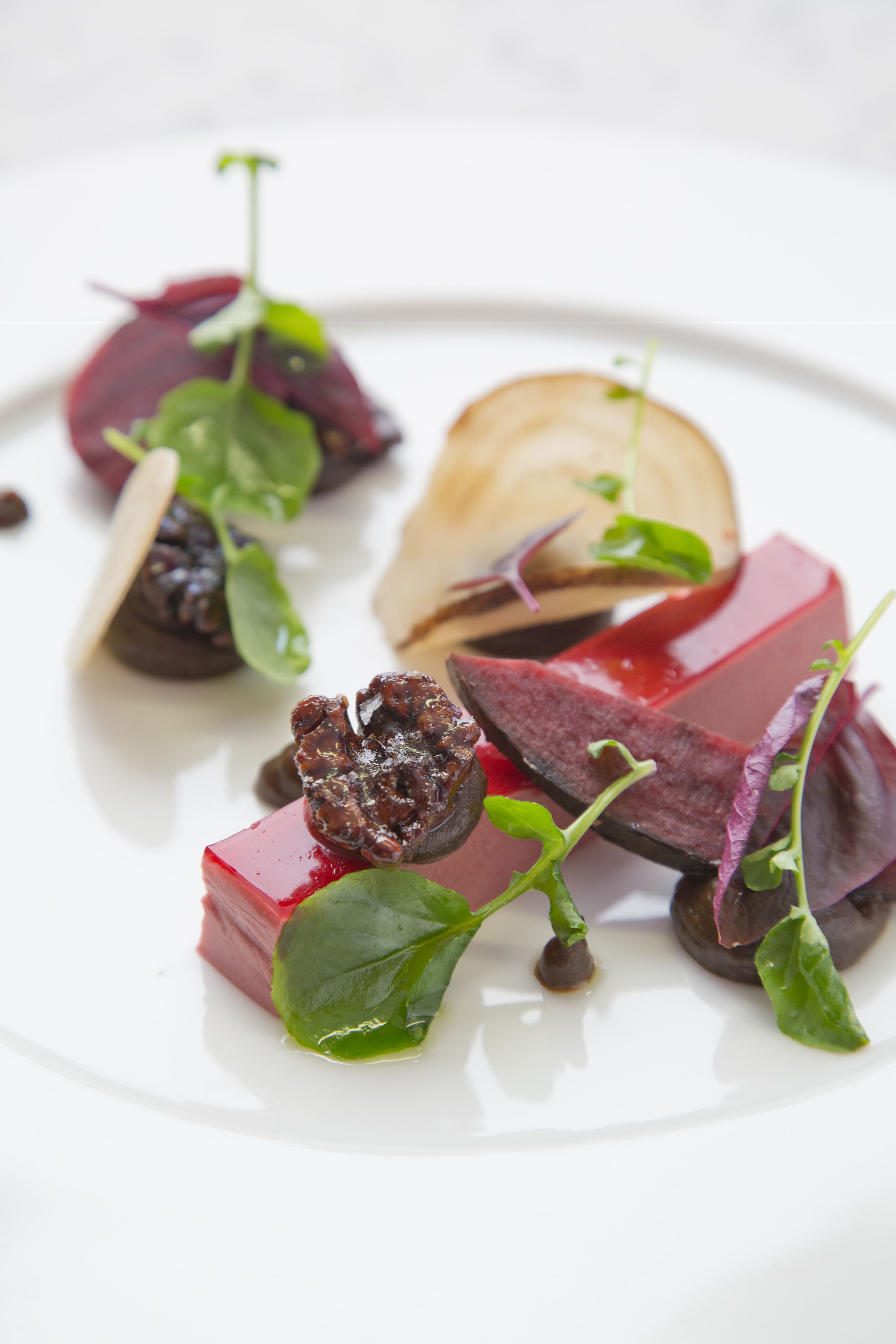 Une assiette blanche contenant divers aliments, notamment des betteraves, des légumes verts et un morceau de pain.